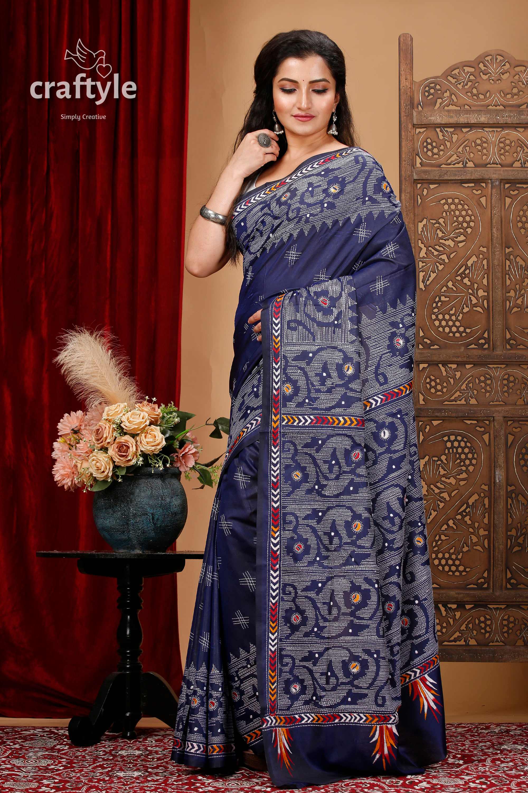 a woman in a blue sari standing in front of a red curtain