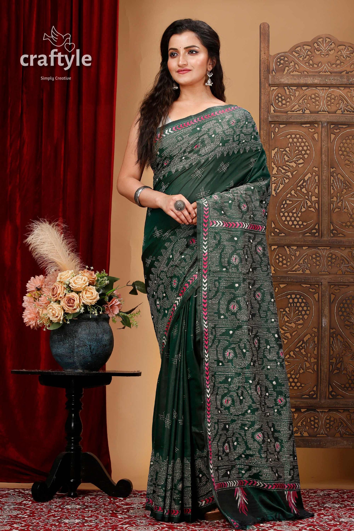 a woman in a green sari standing in front of a red curtain