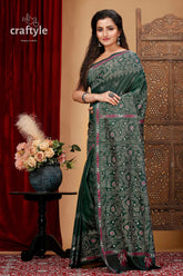 a woman in a green sari standing in front of a red curtain