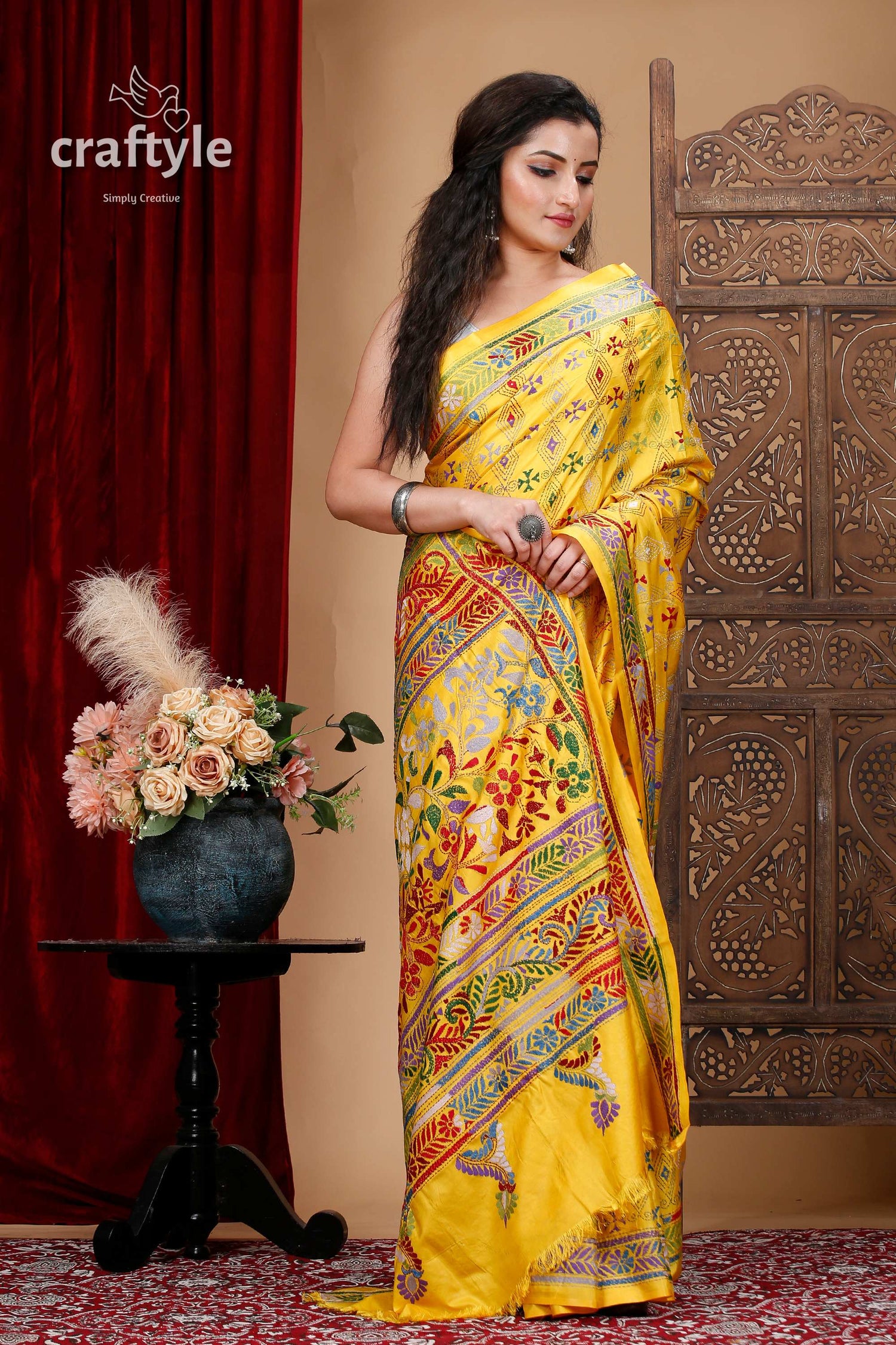 a woman in a yellow sari standing in front of a red curtain