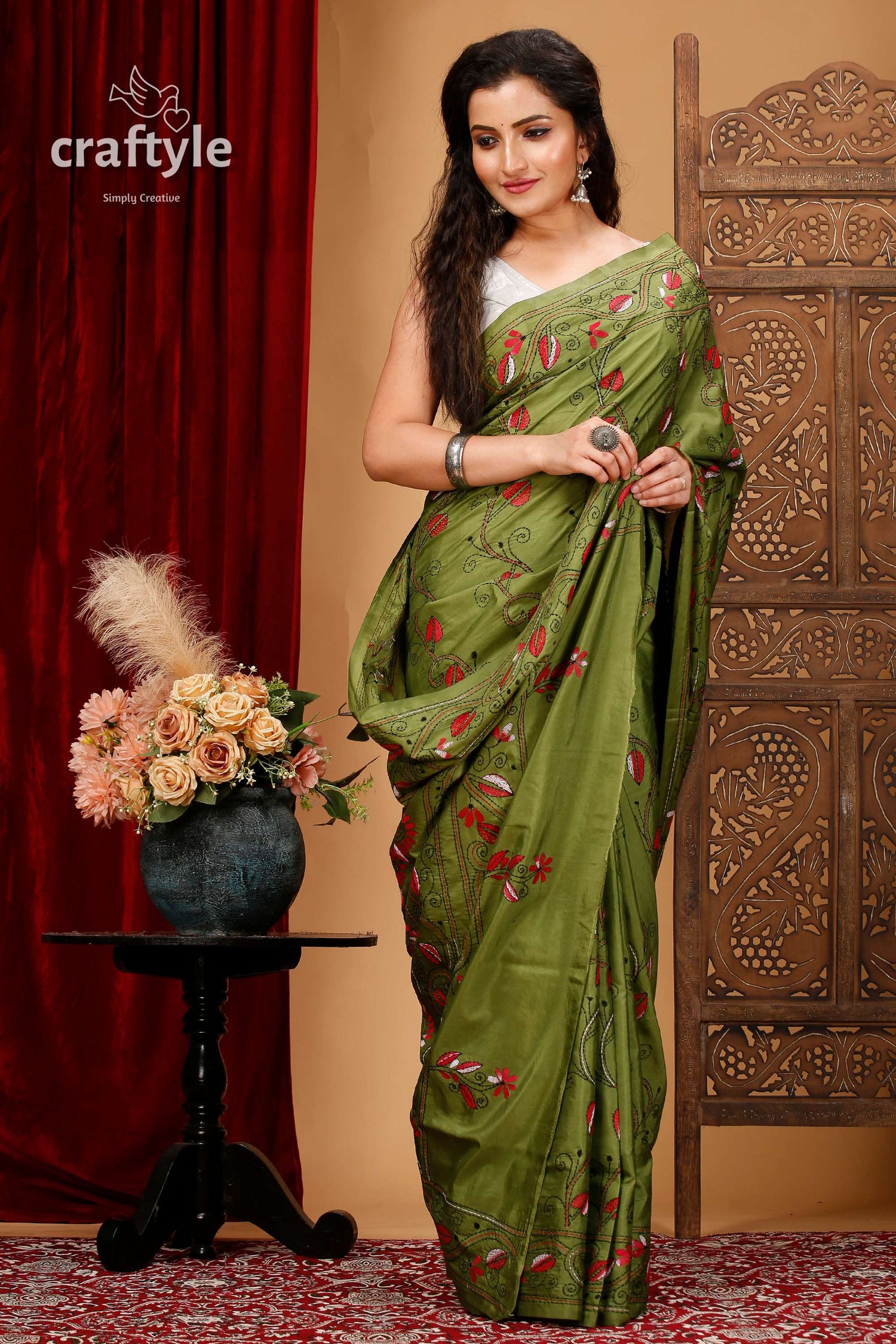 a woman in a green sari standing in front of a red curtain