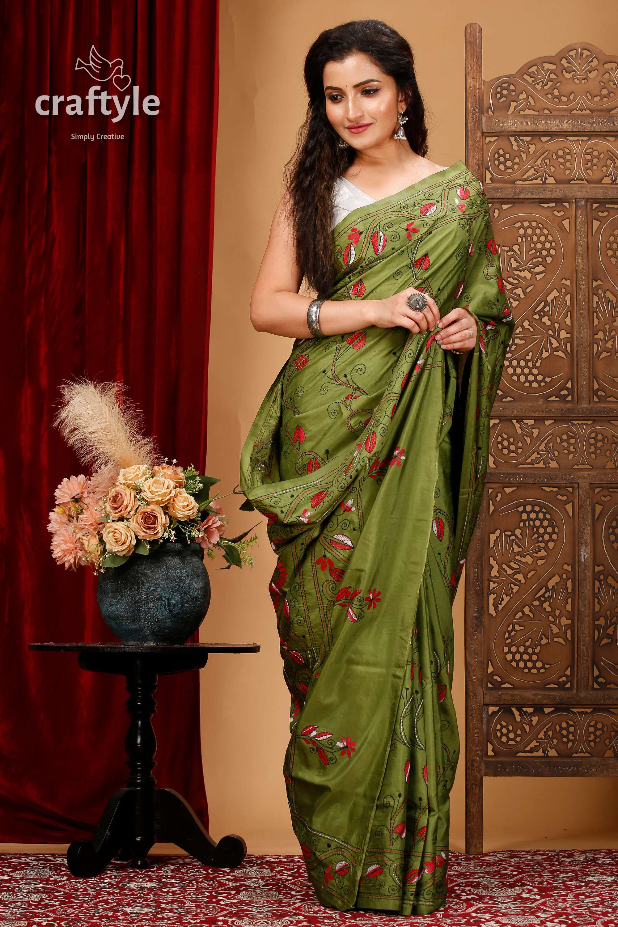 a woman in a green sari standing in front of a red curtain